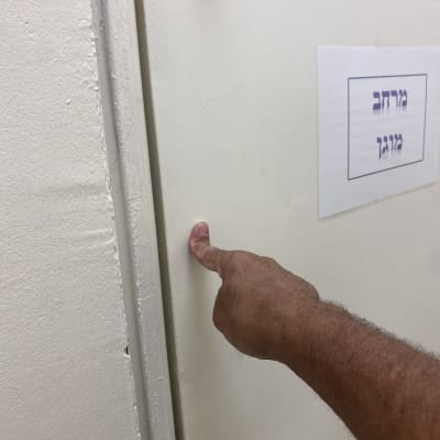 אצבע לוחצת על דלת עם שלט בעברית