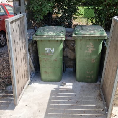 שני פחי אשפה ירוקים ליד גדר עץ