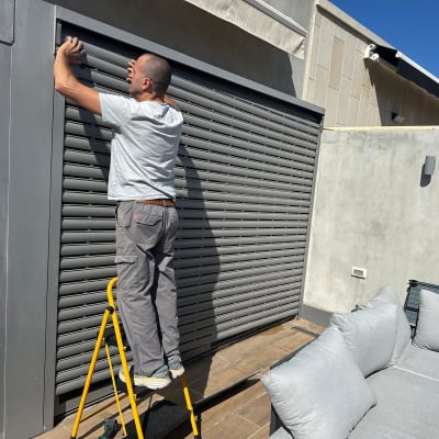 אדם מתקין תריסים על סולם ליד קיר חיצוני