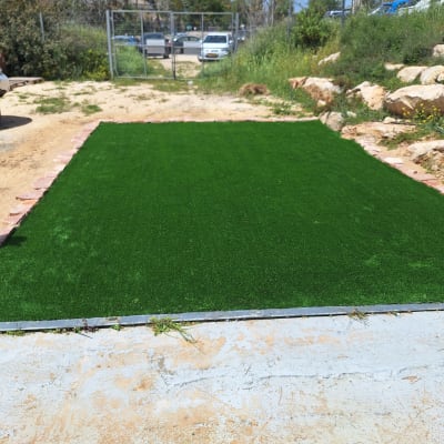 דשא סינתטי מותקן בחצר עם צמחייה מסביב
