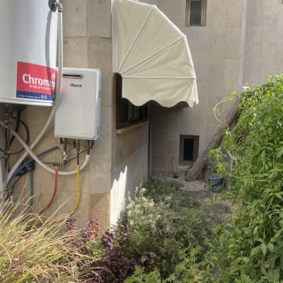 סוכך לבן מותקן על קיר חיצוני ליד צמחייה