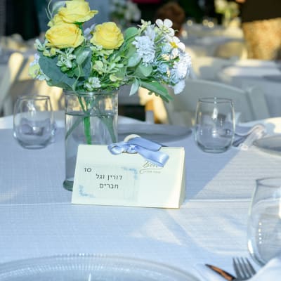 זר פרחים צהובים ולבנים על שולחן עם כרטיס מקום