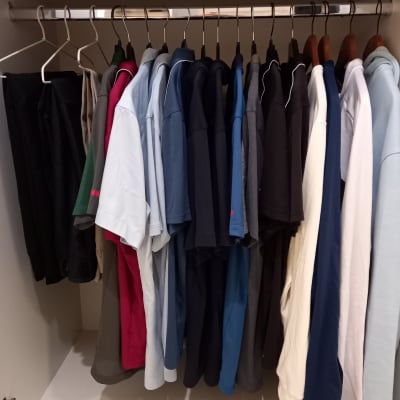 חולצות תלויות בארון על קולבים מסודרים לפי צבעים