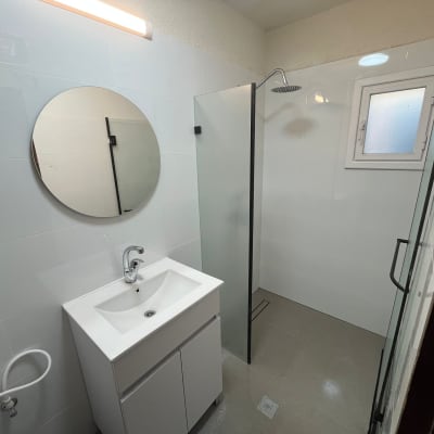 חדר אמבטיה משופץ עם מקלחון, כיור ומראה עגולה