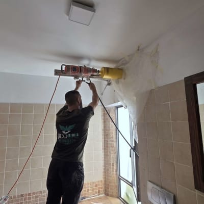 אדם קודח תקרה בחדר אמבטיה עם מקדחה