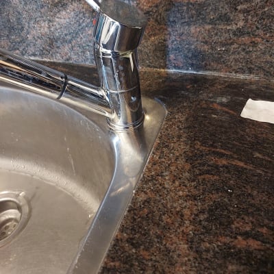 ברז נירוסטה על משטח שיש כהה ליד כיור