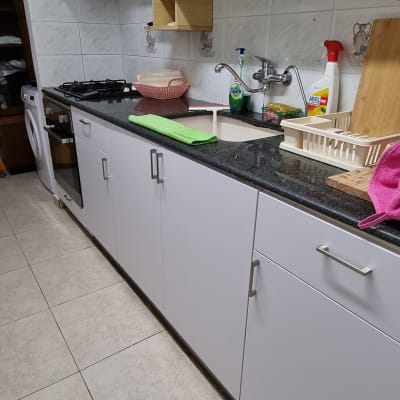 מטבח עם ארונות לבנים, כיור וברז, חומרי ניקוי