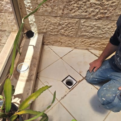 אדם כורע ליד פתח ניקוז ברצפה