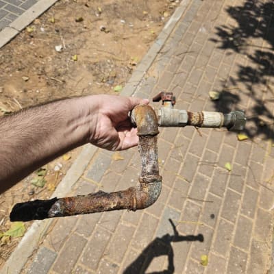 צינור חלוד מוחזק ביד על רקע מדרכה