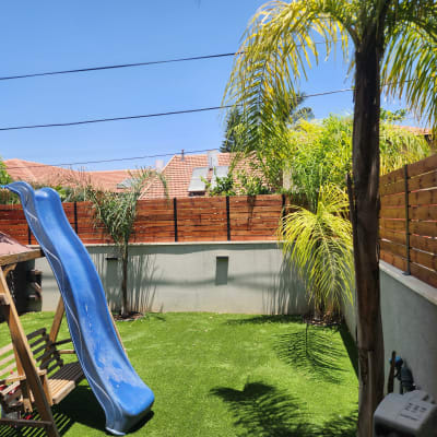 מגלשה כחולה בגינה עם דשא סינתטי וגדר עץ