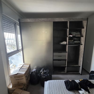 ארון בגדים עם מדפים ותכולה, קופסאות קרטון ליד החלון