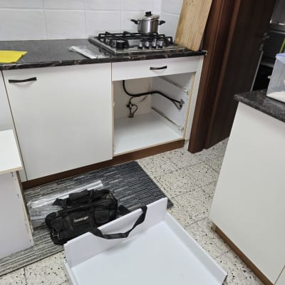 מטבח עם כיריים, סיר, ארון פתוח וכלי עבודה על הרצפה.