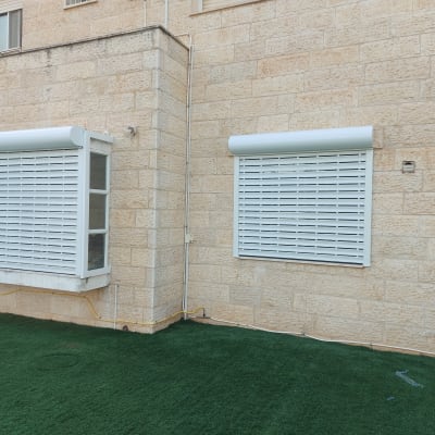 תריסי אלומיניום לבנים על קיר אבן