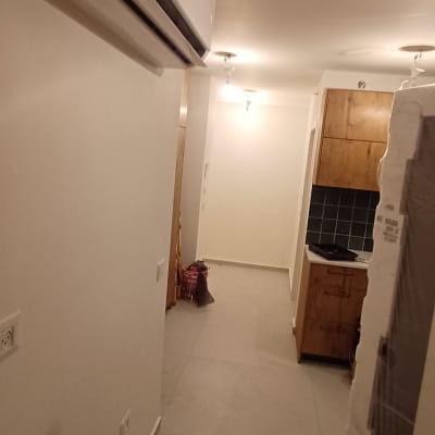 קירות פנים צבועים בלבן בדירה ריקה עם מזגן ומטבח ברקע