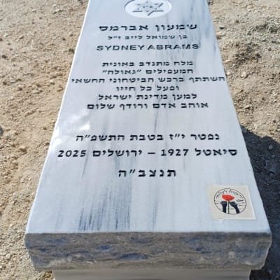 מצבה עם כיתוב בעברית ואנגלית על רקע אדמה