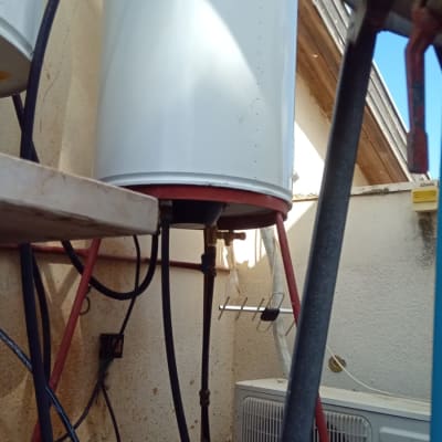 דוד שמש לבן על מתקן מתכת אדום עם צינורות מחוברים