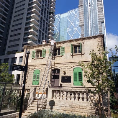 אדם על סולם ליד בניין עם תריסים ירוקים