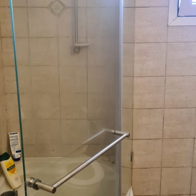 מקלחון עם דלת זכוכית, בקבוקי שמפו וסבון