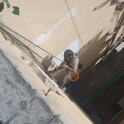 אדם עם קסדה עובד בגובה על קיר בניין