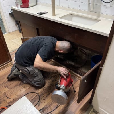 אדם עובד מתחת לכיור עם כלי עבודה אדום