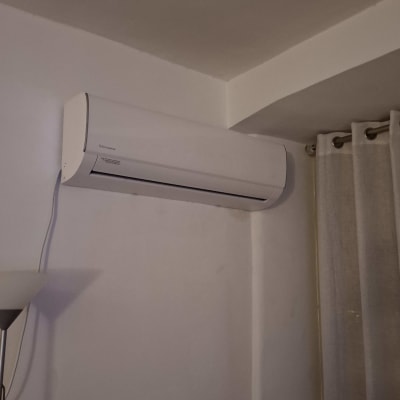 מזגן מותקן על קיר ליד וילון וצמחייה