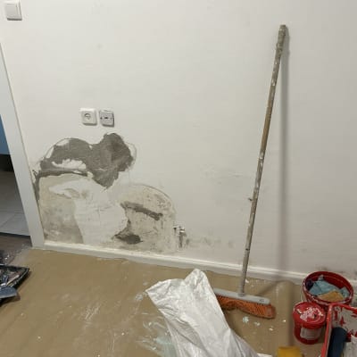 קיר עם תיקוני טיח, כלי עבודה ודלי צבע אדום