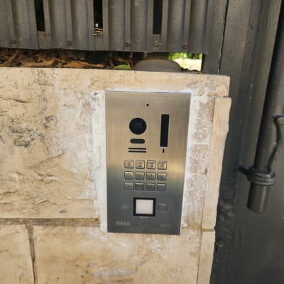 פאנל אינטרקום וקודן משולב מצלמה מותקן בחומת אבן לצד שער