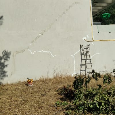 קיר עם סדקים ותיקוני איטום, סולם ודלי צבע