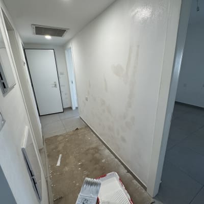 אדם צובע קיר במסדרון עם מברשת ורולר