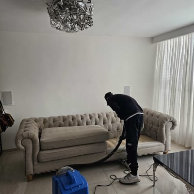 אדם מנקה ספה עם מכונת ניקוי כחולה