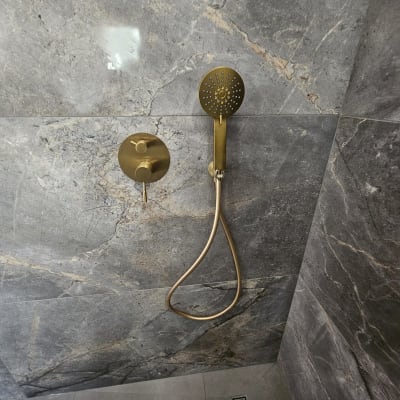 ראש מקלחת מוזהב על קיר שיש אפור