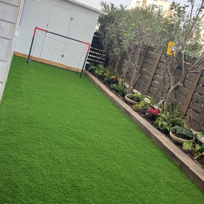 דשא סינתטי עם עציצים ופרחים ליד גדר