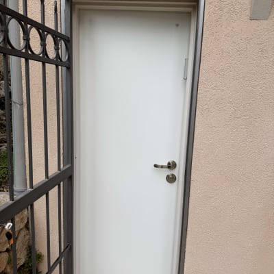 דלת לבנה עם ידית מתכת ליד גדר ברזל