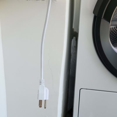 תקע חשמלי לבן תלוי ליד מכונת כביסה