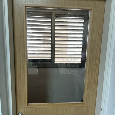 דלת עץ עם חלון זכוכית ומאחוריו תריסים