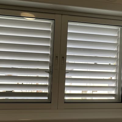 חלון עם תריסים לבנים פתוחים למחצה