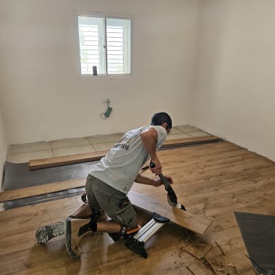 אדם מתקין פרקט עץ בחדר ריק עם חלון