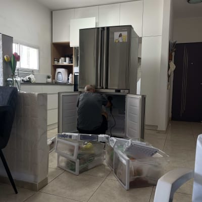 אדם מתקן מקרר עם מגירות פתוחות על הרצפה