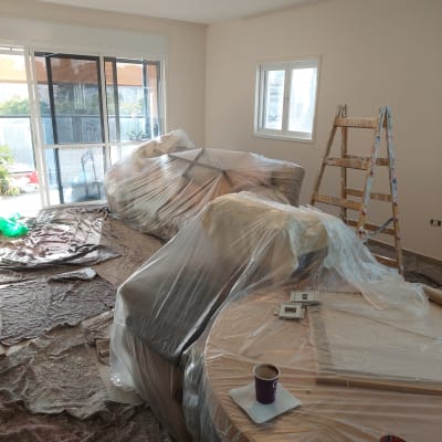 חדר עם רהיטים מכוסים בניילון וסולם לצביעת קירות