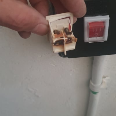 יד מחזיקה שקע חשמלי פתוח ליד מתג קיר