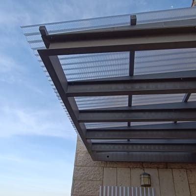 גג מתכת עם לוחות שקופים מחובר לקיר אבן