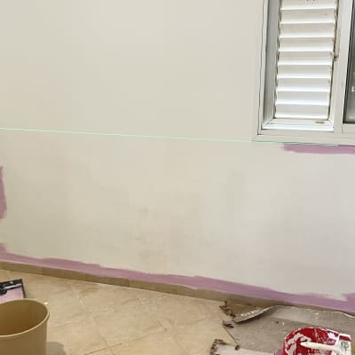 חדר עם קיר צבוע חלקית בצבע ורוד וכלי עבודה לצביעה