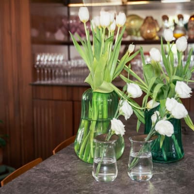 שני אגרטלים ירוקים עם פרחים לבנים על שולחן