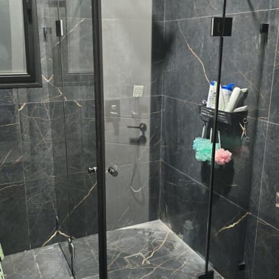 מקלחון זכוכית עם אביזרי רחצה על קיר שיש כהה