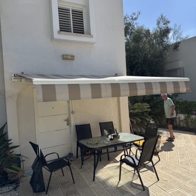 סוכך זרועות מתקפל בדוגמת פסים מעל פינת ישיבה בחצר