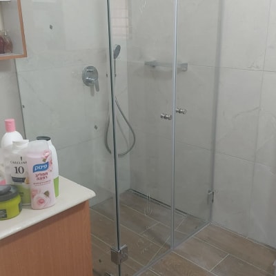 מקלחון זכוכית בחדר אמבטיה עם מוצרי טיפוח על מדף