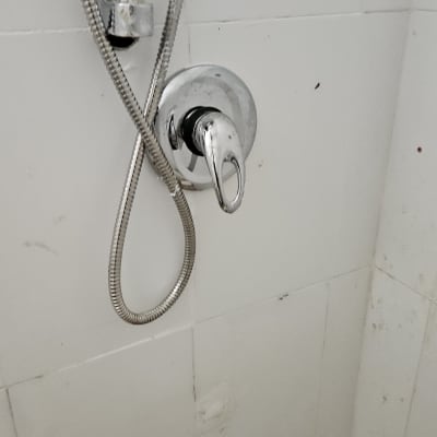 ברז מקלחת עם צינור מתכת על קיר לבן