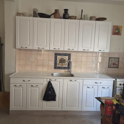 מטבח מוגמר עם ארונות לבנים, משטח עבודה וחיפוי קיר קרמיקה