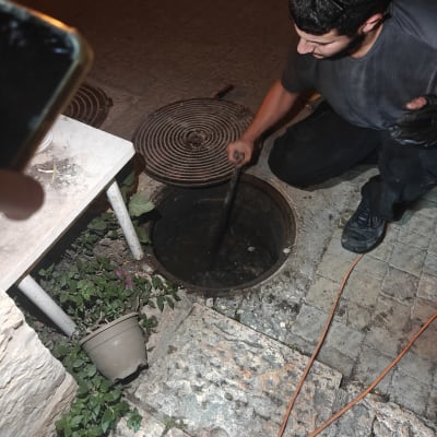 אינסטלטור מבצע פתיחת סתימה בשוחת ביוב בחצר בשעות הלילה