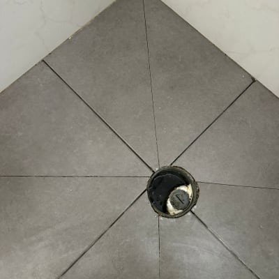 ניקוז מים ברצפת אריחים אפורה עם סימני רטיבות